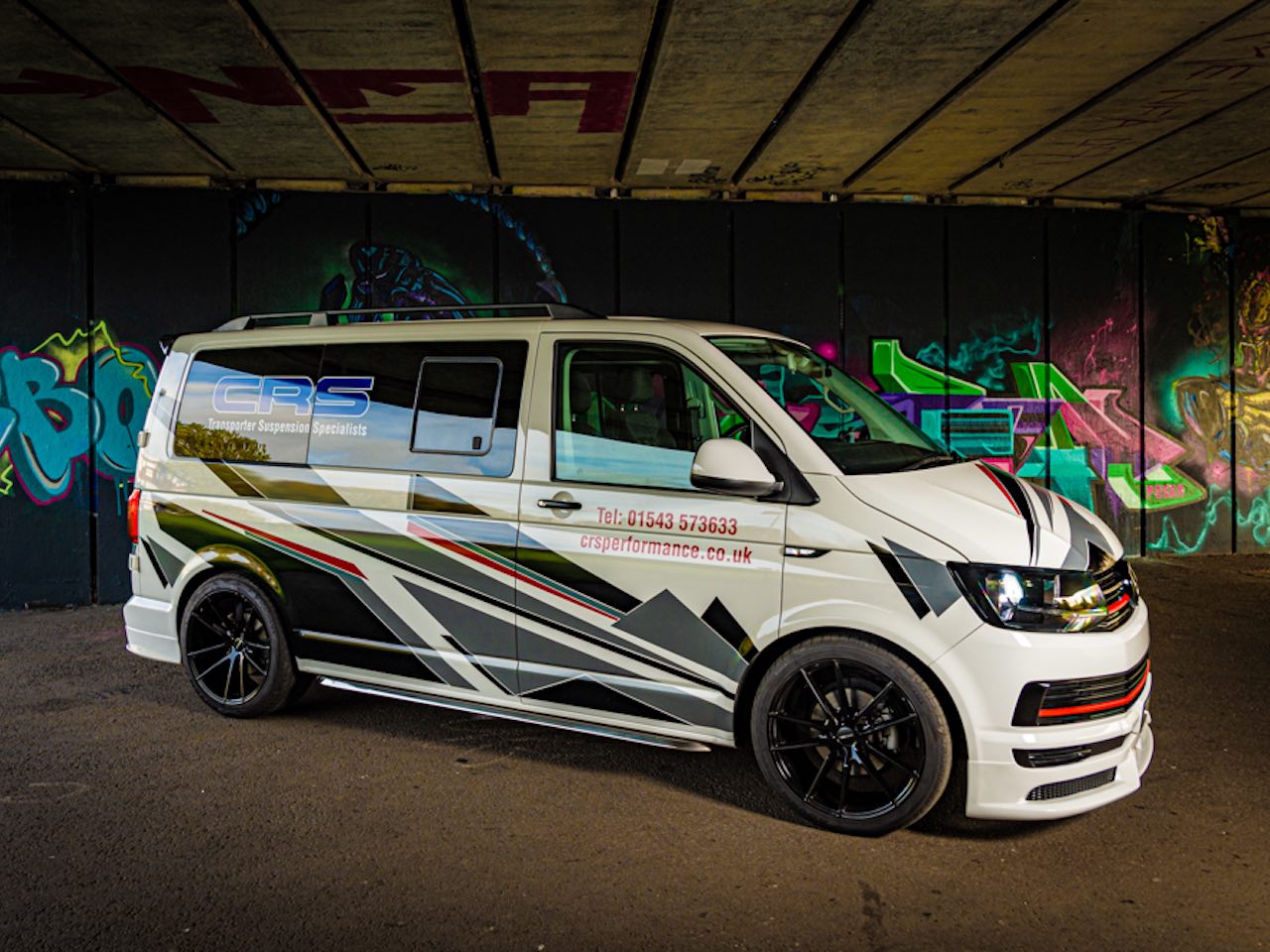 Styled van parked under graffiti-covered bridge.